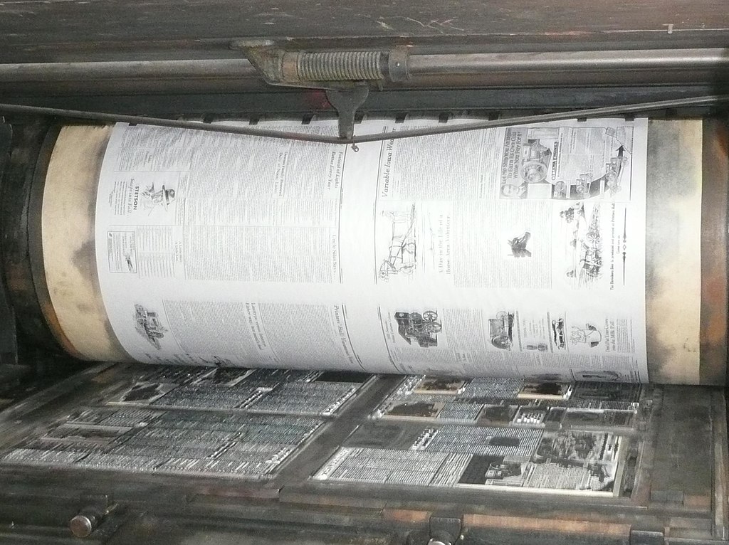 From a bygone era: an old printing press in operation, with freshly printed copy on the cylinder. (Photo credit: Douglas W. Jones/Wikimedia Commons)